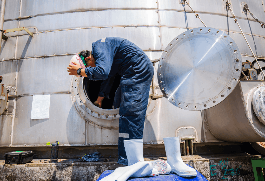 A male worker with a helmet and safety uniform entering a confined space on site which has confined space rescue plans in place.